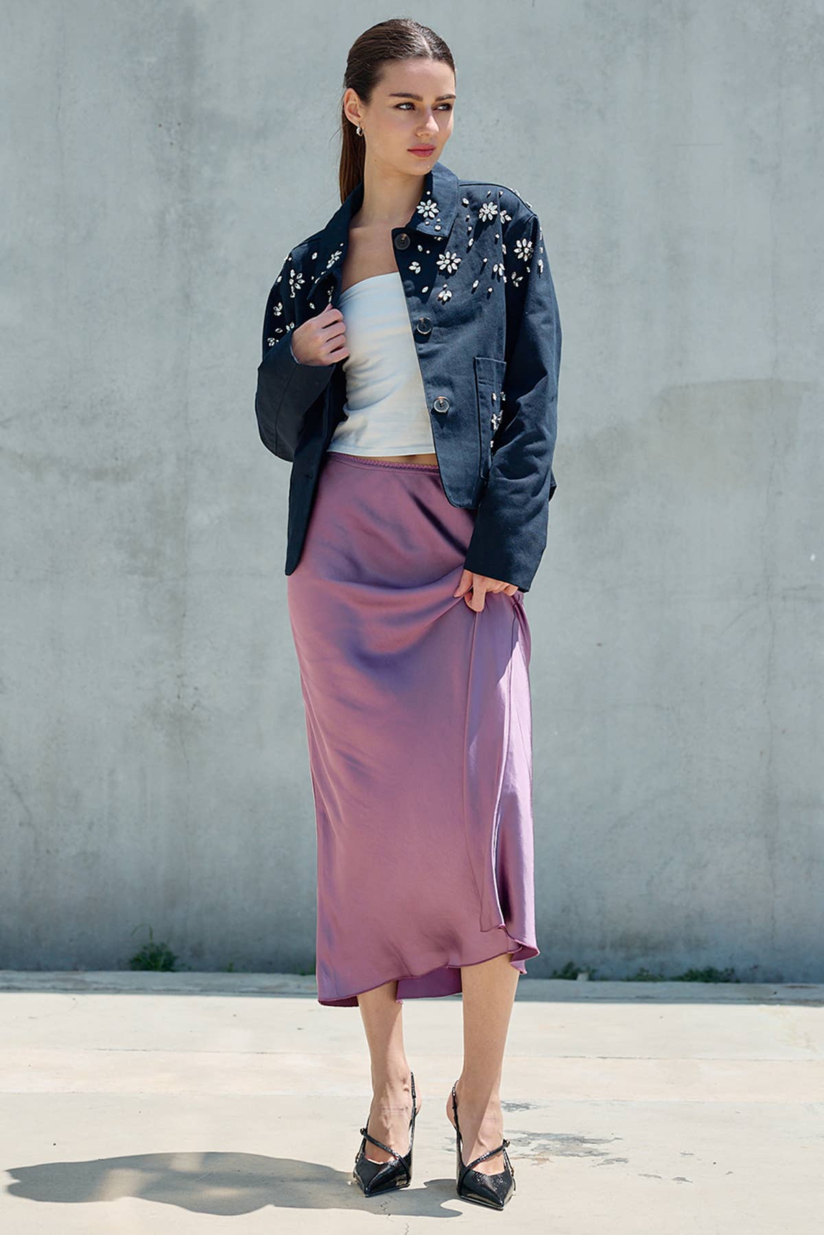 Woman wearing a mauve satin midi skirt with a flowing silhouette denim jacket and heels