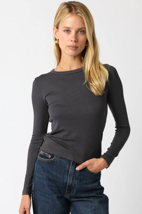 Woman wearing a fitted dark long sleeve top with a crew neckline paired with blue jeans in a casual pose