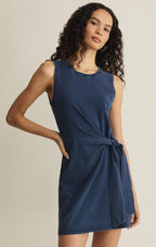 Woman wearing sleeveless navy blue jersey mini dress with wrap side tie detail in neutral background