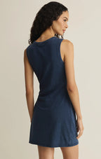 Woman wearing sleeveless navy blue jersey mini dress with a crew neckline and tie side detail from behind