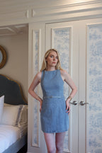Woman wearing sleeveless denim mini dress standing in bedroom with white and blue patterned doors behind her