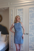 Woman wearing sleeveless fitted denim mini dress standing in a bedroom with white paneled doors behind her