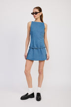 Woman wearing a sleeveless denim mini dress with a fitted waist and short skirt, styled with black loafers and sunglasses