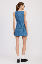 Woman wearing sleeveless denim mini dress with belt detail, styled with white socks and black shoes from back view.