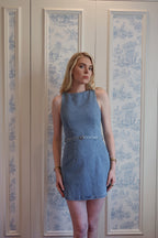 Woman wearing sleeveless blue denim mini dress standing indoors against patterned wall panels