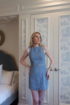Woman wearing sleeveless denim mini dress standing in bedroom with patterned closet doors behind her