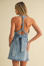 Woman wearing open-back denim mini dress with twisted strap and tied waist, showing casual women's clothing style.