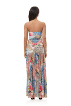 Woman wearing a strapless long patchwork dress with floral and abstract patterns in soft pastel colors