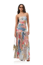 Woman wearing strapless maxi dress with colorful floral and patchwork pattern holding beaded handbag