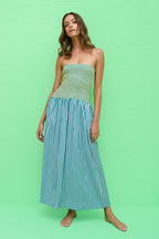 Woman wearing a strapless smocked dress with striped skirt standing barefoot against a green wall background