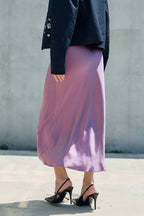 Woman wearing a lilac satin midi skirt with black heels and a dark jacket