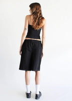 Woman wearing black eco-denim jorts with elastic waist paired with black tank top, white socks, and black shoes.