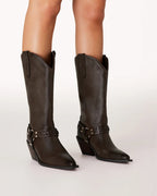 Women's dark brown mid-calf leather boots with pointed toes and decorative straps on a neutral background