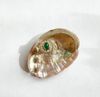 Gold hexagon ring with a green emerald center and surrounding diamonds displayed in a shell on white background