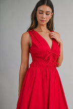 Woman wearing a sleeveless bright red midi dress with gathered waist and tie details on the bodice