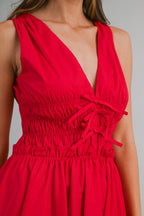 Woman wearing sleeveless red dress with deep V-neck and ruched waist detail in women's clothing