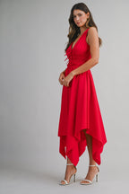 Woman wearing sleeveless red midi dress with handkerchief hem and white high heel sandals against gray background