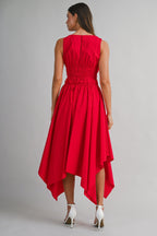 Woman wearing a sleeveless red midi dress with an asymmetrical hem and gathered waist, paired with white heels