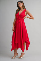 Woman wearing a sleeveless red midi dress with a handkerchief hem and white high-heeled sandals posing against gray background