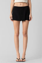 Woman wearing black tailored wrap skort paired with sandals, showcasing minimalist women's clothing style.