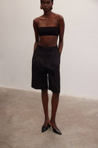 Woman wearing black high-waisted knee-length shorts and a black bandeau top in a minimal studio setting