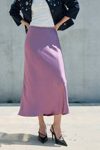 Woman wearing a lilac satin midi skirt with black heels and a dark jacket
