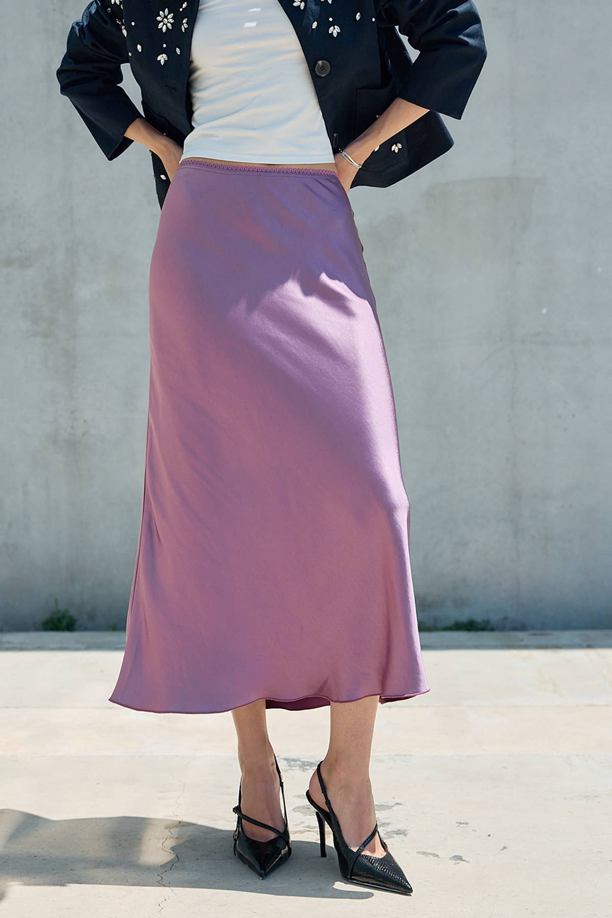 Woman wearing a lilac satin midi skirt with black heels and a dark jacket