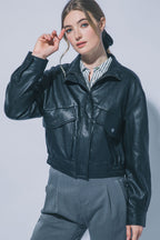 Woman wearing black faux leather jacket with front flap pockets and zip closure over striped shirt and gray pants