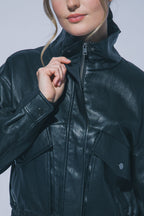 Woman wearing black faux leather jacket with high collar and large front pockets, holding zipper near chin