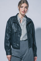 Woman wearing black faux leather jacket with front pockets over striped shirt and gray pants against light background