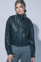 Woman wearing a black faux leather jacket with large front pockets and a high funnel collar in a studio setting
