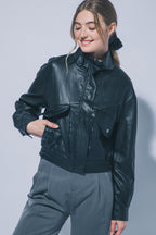 Woman wearing black faux leather funnel jacket with large pockets and gray pants smiling with eyes closed