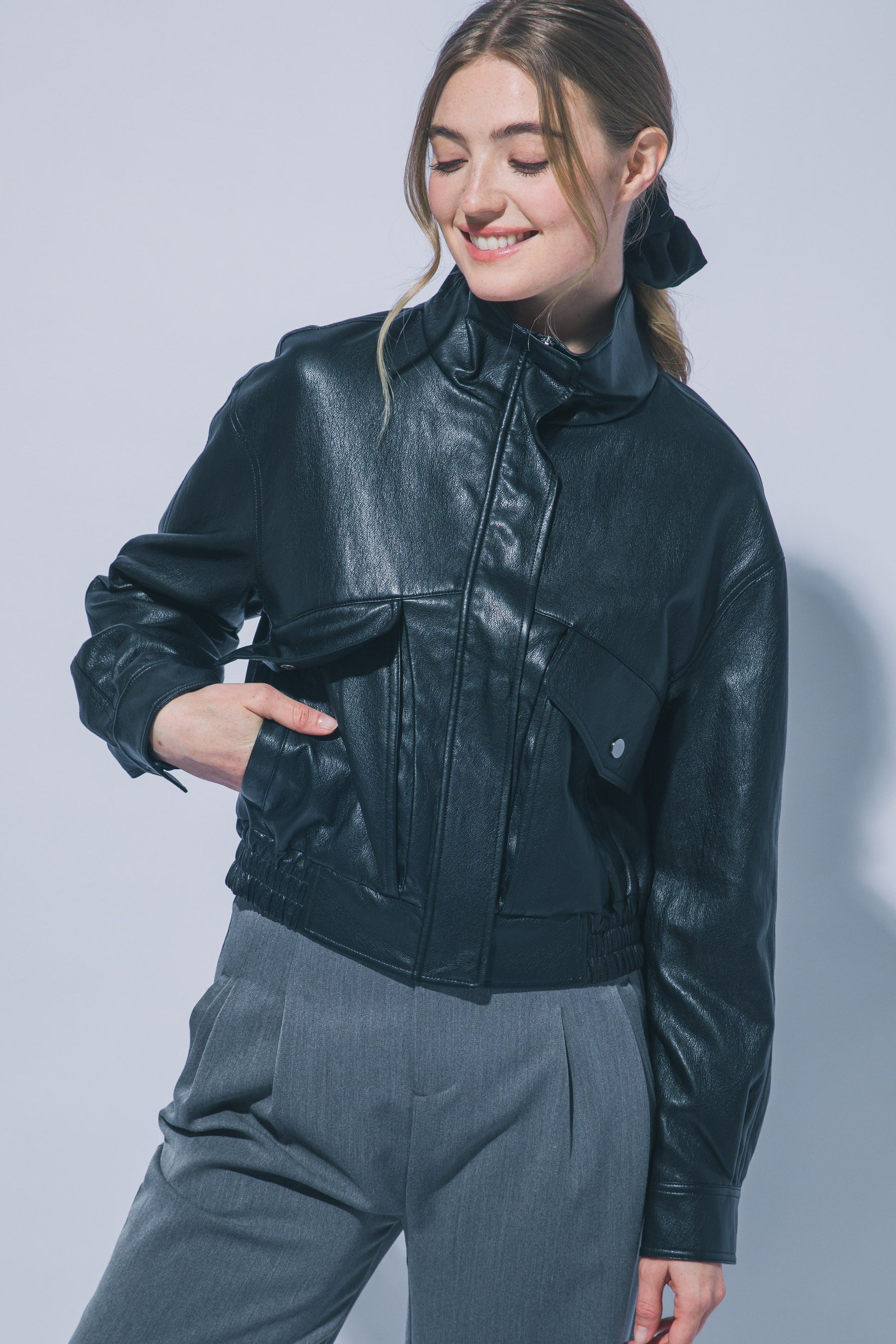 Woman wearing black faux leather funnel jacket with large pockets and gray pants smiling with eyes closed