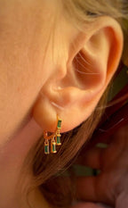 Close-up of an ear wearing a delicate gold earring with small dangling green gemstones for women’s fashion.