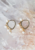 Gold hoop earrings with small dangling white pearls on a textured crystal surface women's accessory