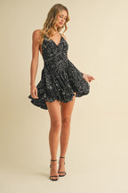 Woman wearing a black floral ruffle romper with a V-neck and flared skirt in a light studio setting
