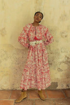 Woman wearing a bohemian long dress with red patterns and a white woven belt in a rustic setting