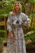 Woman wearing a patterned bohemian long dress with balloon sleeves standing among tropical plants in women's clothing.