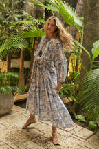 Woman wearing a flowing bohemian maxi dress with blue patterns, standing in a lush tropical garden setting