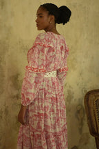 Woman wearing a long patterned maxi dress with red and white details and a braided belt in a rustic setting