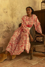 Woman wearing a patterned bohemian maxi dress sitting on a wicker chair in a rustic room setting