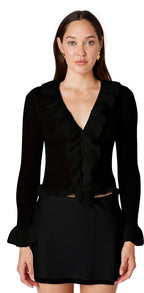 Woman wearing a black loosely knit cardigan with ruffled neckline and sleeve openings, paired with a black skirt.