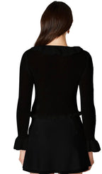 Woman wearing a black loosely knit cardigan with ruffled neckline and sleeve openings, shown from the back