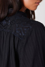Close-up of black woven cotton women's shirt with intricate embroidered back detail and scallop trim on shoulders
