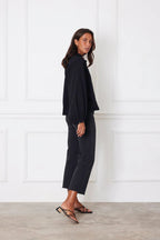 Woman wearing a black long-sleeve blouse with billowy sleeves and black cropped pants in a minimalist room