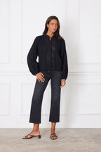 Woman wearing a black blouse with billowy sleeves and embroidery paired with black cropped jeans and sandals.