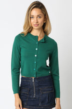 Woman wearing a green cropped knit cardigan with buttons paired with a dark denim zip-up skirt in women's clothing.