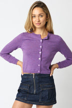 Woman wearing a fitted purple button-down cropped knit cardigan paired with a dark denim mini skirt