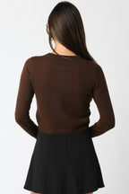 Woman wearing a fitted brown knit cropped cardigan with long sleeves and a black skirt, shown from the back