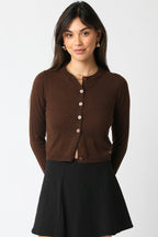 Woman wearing a brown cropped knit cardigan with buttons and a black skirt, styled for women's clothing.